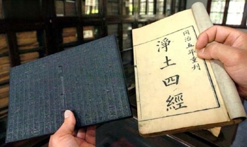 Hands holding a black woodblock printing plate with carvings of Chinese characters and a book