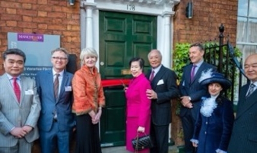 A group of formally dressed individuals posing in front of  the Lee Building's green door outside cutting a red ribbon